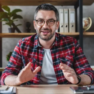 smiling-young-businessman-sit-at-desk-talk-on-webcam-having-video-call-or-conversation-with-client-1.webp